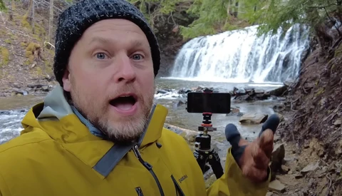 Content creator recording at a waterfall with smartphone mounted on tripod.