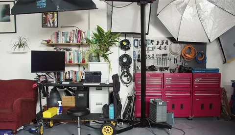 Well-organized photography studio workspace with red tool cabinets, lighting equipment, and shelving along white walls.