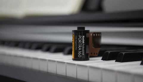 Kodak Portra 160 film canister placed on piano keys with blurred background.