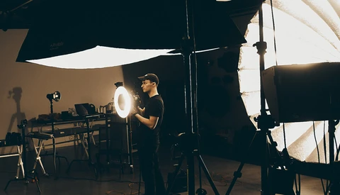 Photographer adjusting a large circular ring light on a studio set with multiple lighting rigs and diffusion panels.
