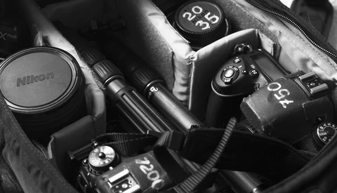 Collection of Nikon DSLR cameras and lenses arranged in a camera bag, shot in black and white.