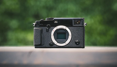 Black mirrorless camera with textured grip displayed against blurred green background.