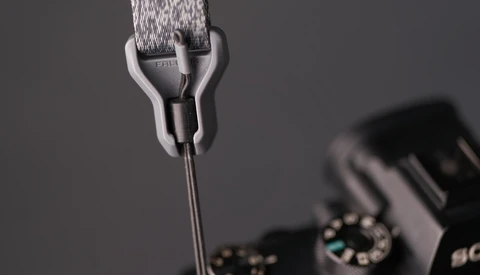 Close-up of a camera strap attachment mechanism with gray fabric strap and metal connector hardware.