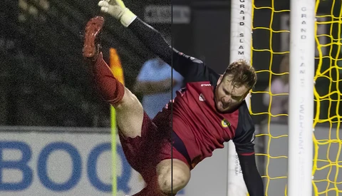 Soccer goalkeeper in maroon jersey diving horizontally to make a save, with yellow goal net visible behind.