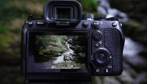 Camera rear LCD screen displaying a forest stream photograph with rocks and flowing water.
