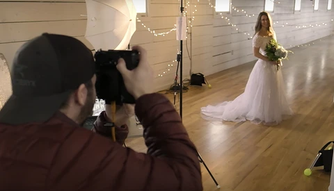Photographer shooting a bridal portrait of a woman in a white wedding dress holding a bouquet in an indoor venue.
