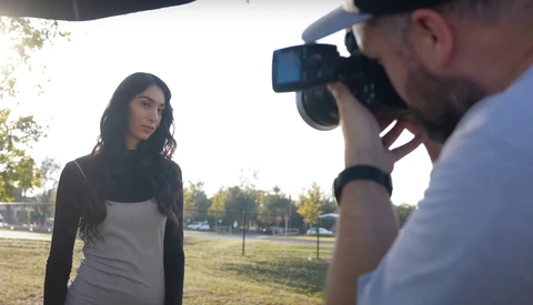 Photographer with DSLR camera photographing woman in casual clothing outdoors during golden hour.