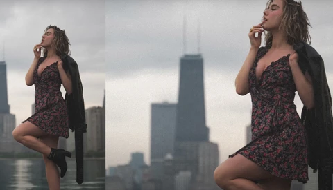 Woman in patterned dress and black cardigan posing against urban skyline with tall buildings.