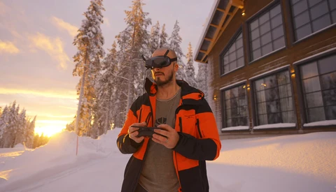 Man in bright orange jacket and dark cap standing in snowy landscape at golden hour.
