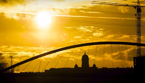 Silhouetted cityscape with arched bridge and cathedral dome against golden sunset sky.