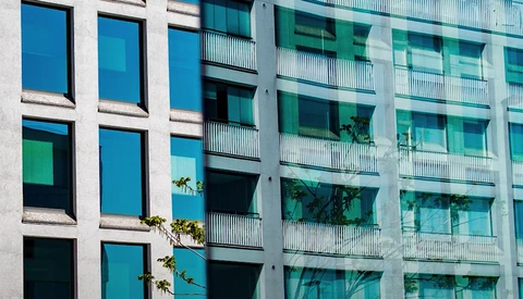 Modern residential building facade with contrasting blue and teal windows arranged in a grid pattern, separated by white concrete columns.