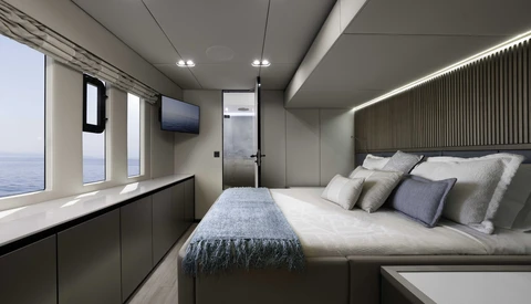 Modern luxury yacht cabin with panoramic ocean views, queen bed with gray upholstered headboard, and integrated storage cabinetry.