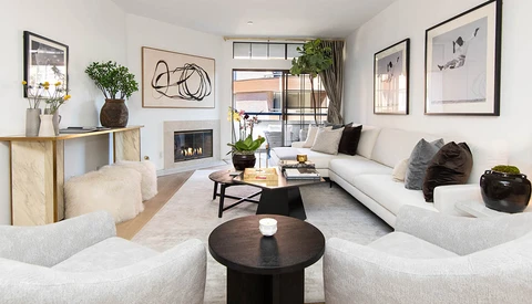 Contemporary living room with neutral furnishings, fireplace, and large windows overlooking urban street.