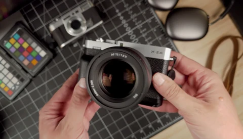 Photographer's hands holding a vintage rangefinder camera with fast lens over a flat lay of photography equipment.