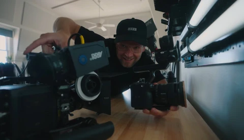 Filmmaker holding a cinema camera indoors, demonstrating equipment in a bright studio space.
