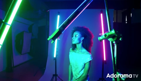 Woman posed among neon tube lights in cyan, green, pink, and blue creating a geometric light setup.