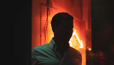 Silhouetted man against warm orange and yellow backlit glow from window or light source.