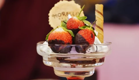 Chocolate-dipped strawberries in a clear glass bowl with a wafer cookie, shot with selective focus and warm studio lighting.