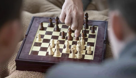 Player's hand moving a wooden chess piece during a game on a purple-bordered board.