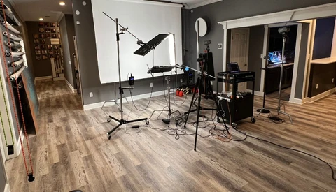 Professional home studio setup with drum kit, microphones, lighting rigs, and acoustic treatment on gray walls.