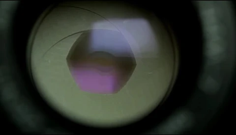Close-up view through a camera lens showing a purple and blue aperture opening with light refraction.