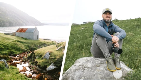 Photographer in hiking gear crouching on a boulder in a misty mountain valley with a stream below.