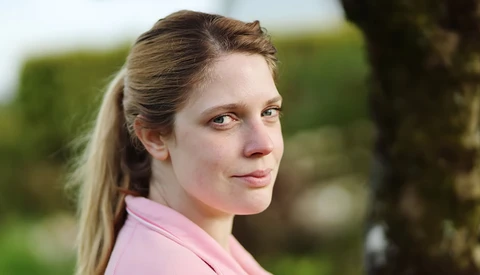 Woman in pink shirt looking over shoulder with soft natural outdoor lighting.