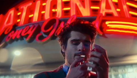 Man smoking cigarette under glowing red neon signage at night.