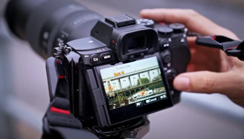 Videographer holding a mirrorless camera with an external monitor displaying a live feed of an interior scene.