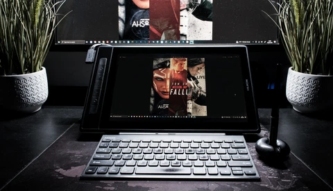 Laptop and desktop monitor displaying film poster designs in a creative workspace with potted plants and microphone.