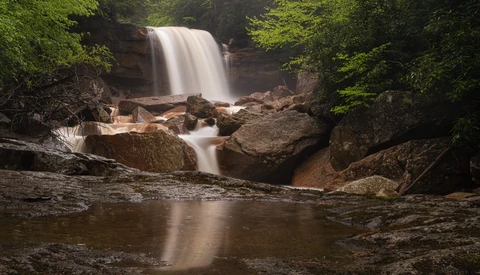 Waterfall cascading over rocky ledge surrounded by dense green forest foliage.