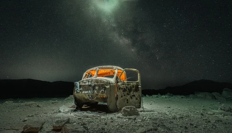 Abandoned rusted truck cab under starry night sky with Milky Way visible overhead.
