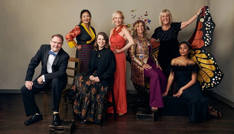Group portrait of eight people in colorful formal and semi-formal attire posed against a neutral background.