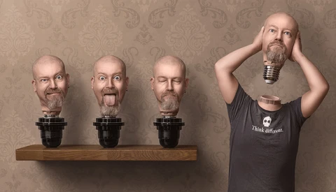Man holding oversized head sculpture while three identical head sculptures sit on wooden shelf against patterned wallpaper.