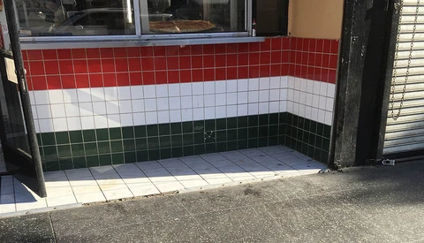 Storefront entrance with red, white, and green horizontal striped tile design on the recessed door area.