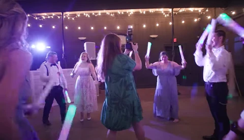 Wedding guests dancing under purple and warm string lights at an indoor reception venue.