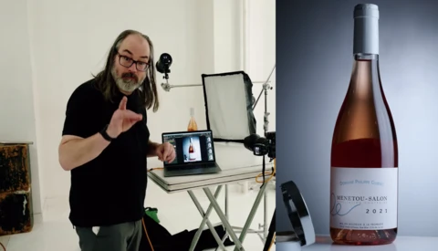Man with long hair and glasses gestures while speaking into a microphone during a video production setup.
