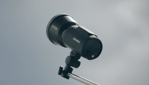 Studio flash or monolight mounted on a light stand against overcast sky.