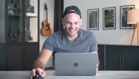 Man smiling at laptop while working at desk in modern home studio.