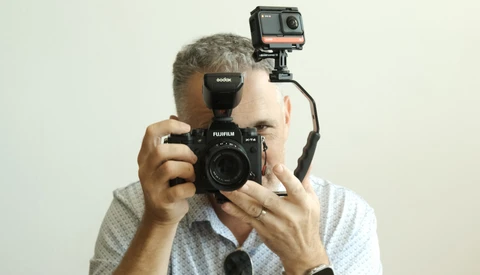 Photographer holding a Fujifilm film camera with an action camera mounted on top.