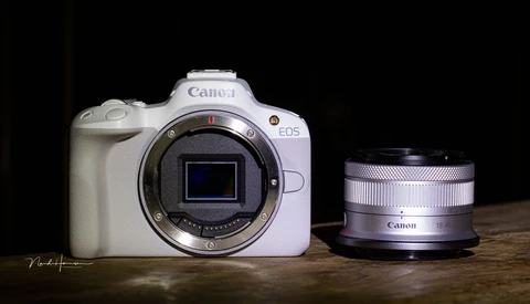 White Canon EOS R50 mirrorless camera body with detached Canon RF-mount lens on wooden surface.