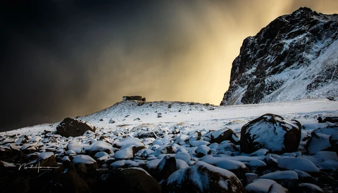 Snow-covered boulders scattered across a frozen landscape beneath a dramatic mountain peak.