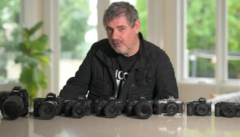 Photographer standing behind nine Nikon DSLR cameras arranged in a line on a white table.