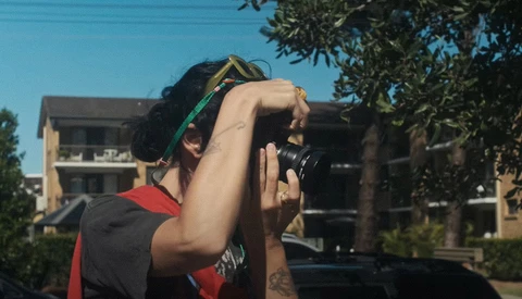 Photographer holding a DSLR camera up to their face while looking through the viewfinder outdoors.