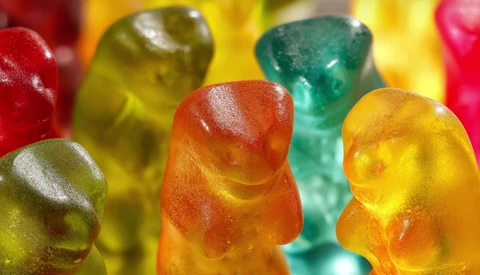 Close-up macro photography of translucent gummy candies in red, yellow, orange, and green colors with shallow depth of field.