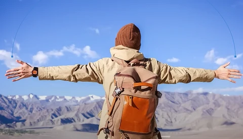Hiker with arms spread wide standing in mountainous desert landscape under clear blue sky.
