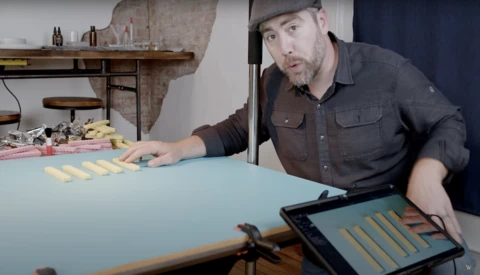 Man in dark shirt demonstrating color swatches on a blue surface with tablet displaying matching palette.