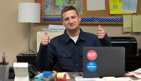 Man giving double thumbs up while sitting at a desk with a laptop.