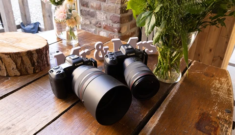 Two mirrorless cameras with telephoto lenses displayed on a wooden table in a studio setting.