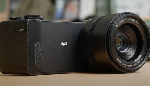 Sigma dp3 compact camera with attached macro lens displayed on neutral surface.